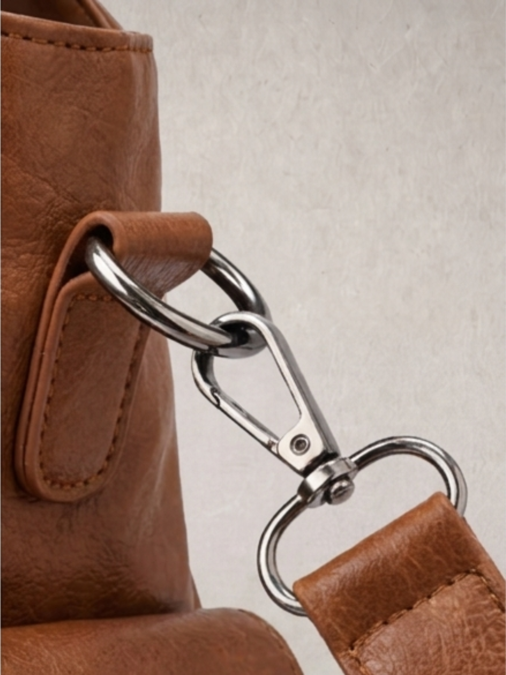 Close-up of the carabiner clip hardware on the L'Elyn camel bag