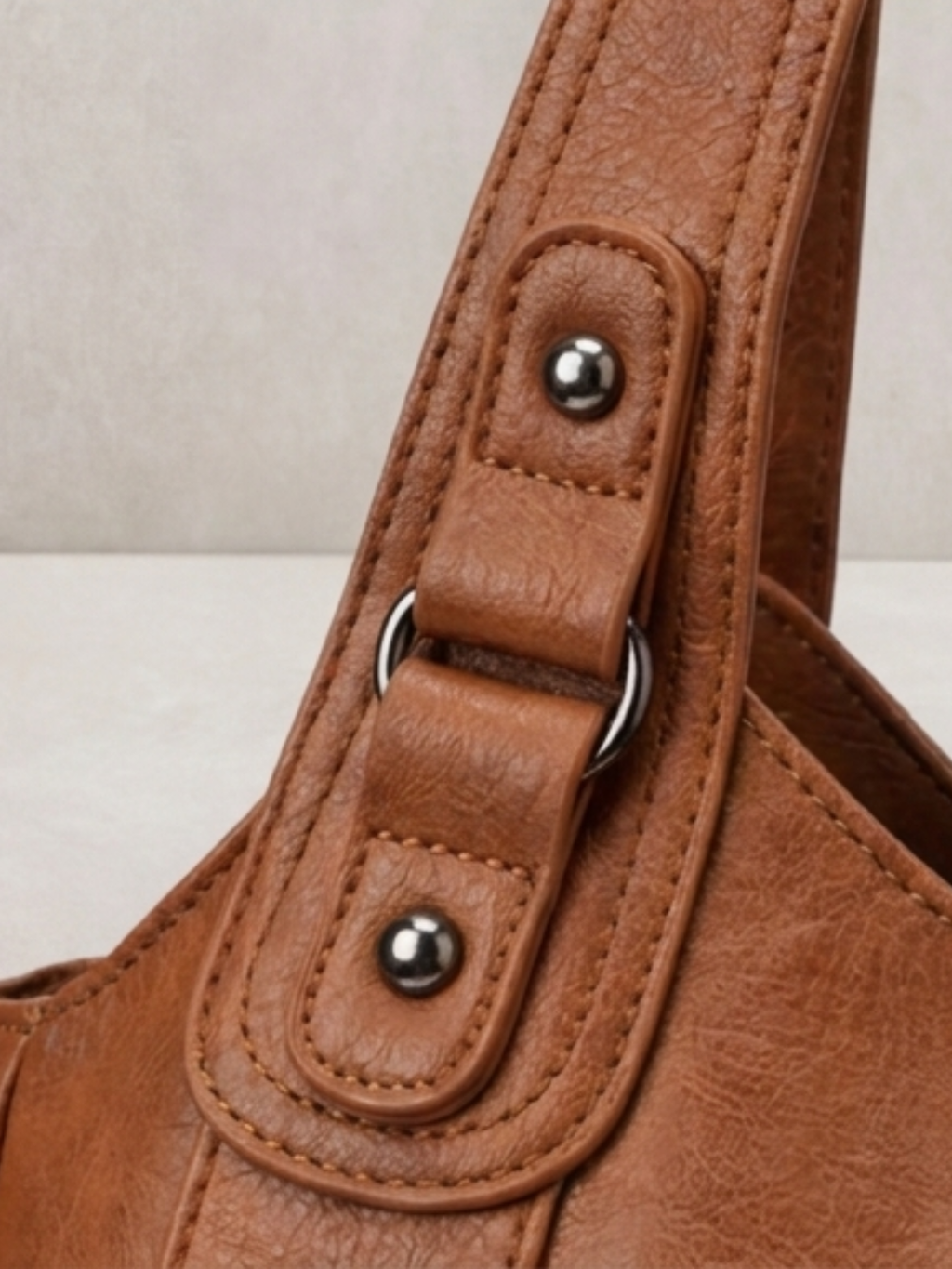 Close-up of the stud and rivet hardware on the L'Elyn camel bag