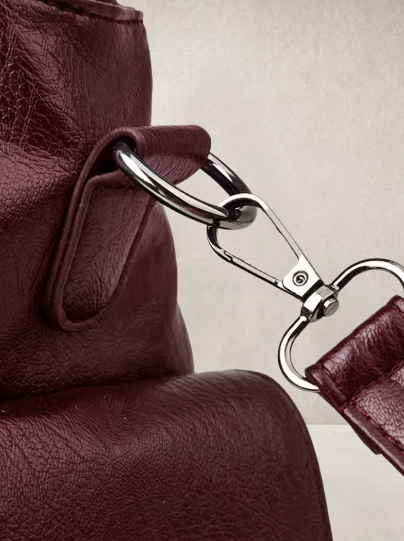 Close-up of the carabiner clip hardware on the L'Elyn burgundy bag