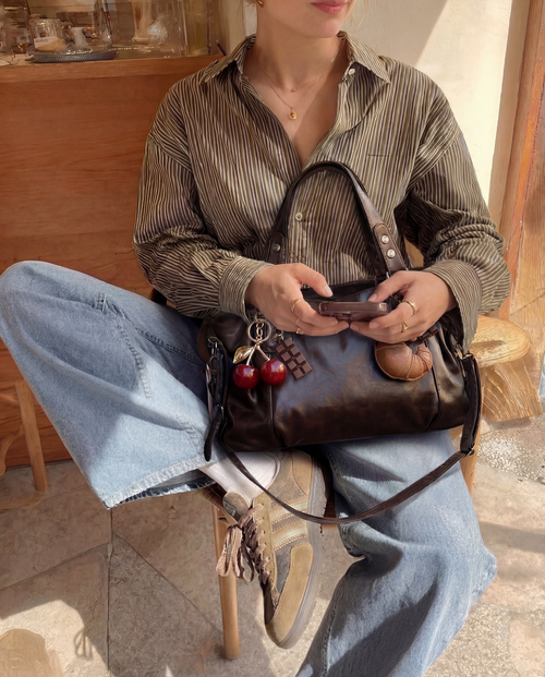 Model holding a burgundy bag with the Cherry Charm attached
