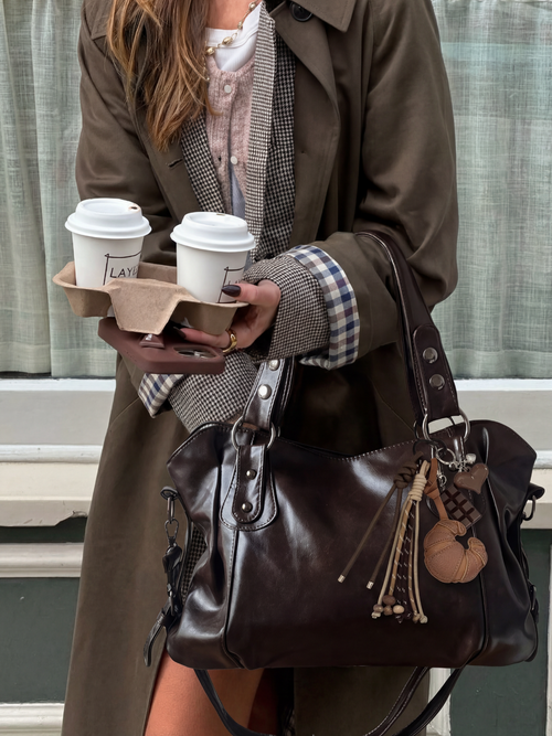 Model holding a coffee cup with the Croissant Charm attached to her bag
