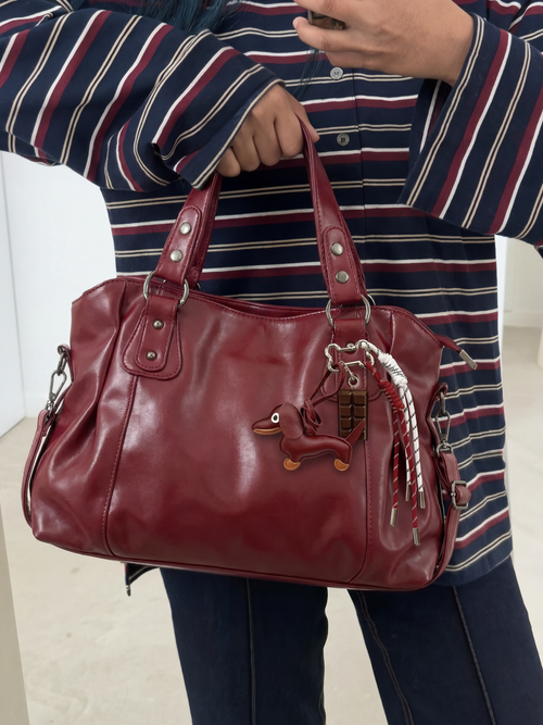 Model holding a burgundy bag with the Dachshund Charm attached
