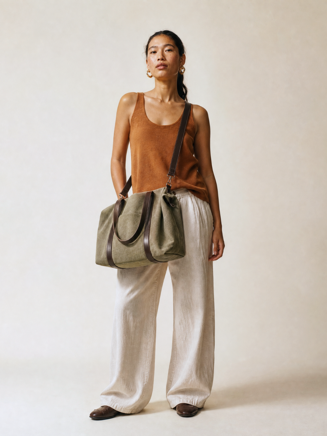 Model walking in cream wide-leg trousers carrying the Le Meline green tote bag on her forearm