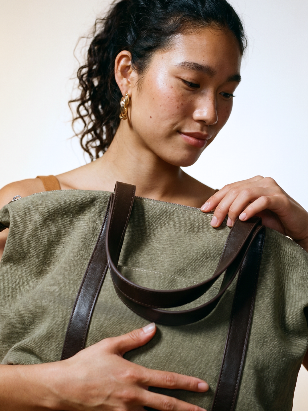 Close-up of a model adjusting the leather strap of the Le Meline green tote bag