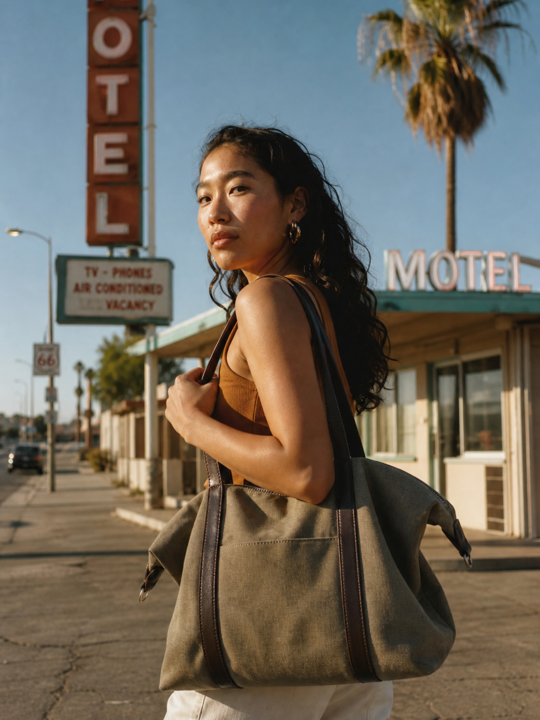 Model walking past a motel storefront carrying the Le Meline green tote bag on her shoulder