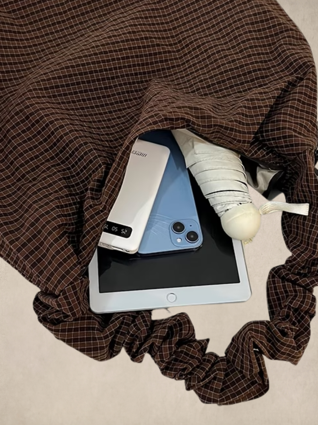 Le Scrunchie brown bag interior showing a phone, power bank, iPad, and umbrella fitting inside