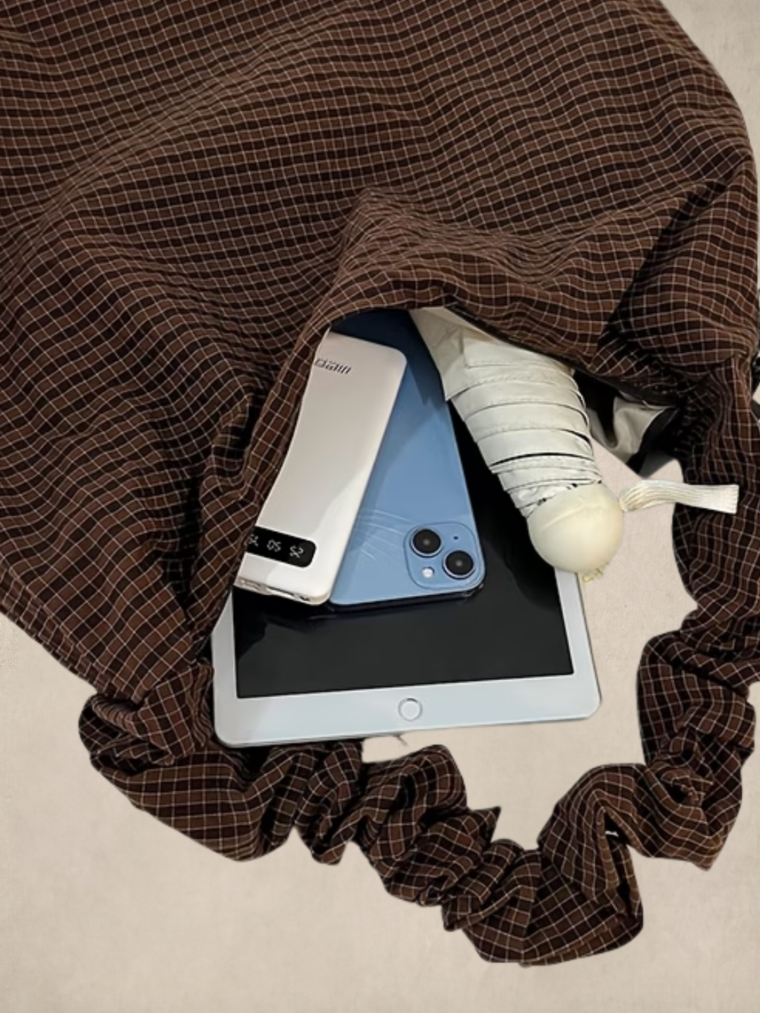 Le Scrunchie brown bag interior showing a phone, power bank, iPad, and umbrella fitting inside